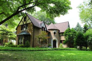 Tudor-style house surrounded by lush greenery with a well-manicured lawn and large trees providing shade.