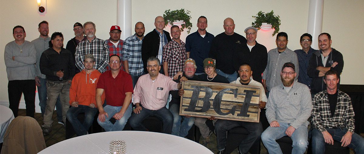 Group of men posing with a "BCF" sign at a casual indoor gathering.