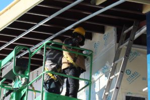 A construction worker in a yellow helmet installing insulation panels on a building from a lift.