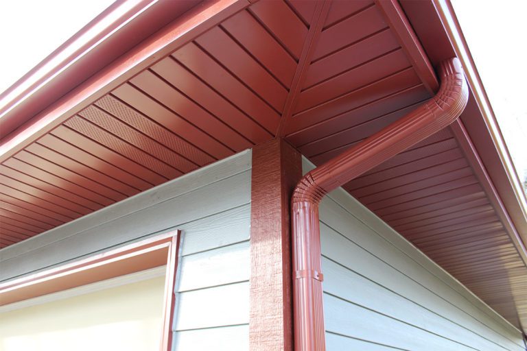 Close-up view of a red house corner showing detailed soffit, fascia, and a matching gutter on the roof.