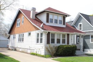 A two-story American Craftsman-style house with white and brown siding, featuring a gabled roof and front porch.