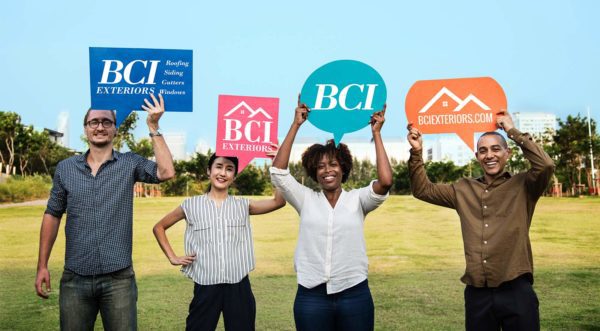 Four diverse adults holding large signs with "BCI Exteriors" logos, smiling in a sunny outdoor setting.