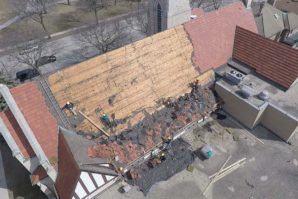 Aerial view of workers repairing a large roof with scattered old tiles on a sunny day.